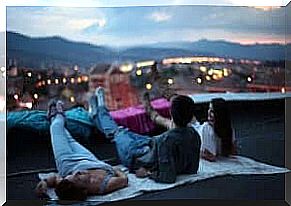 Three friends sit on the edge of a roof of a tall building