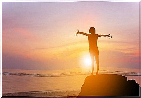 A woman stands with outstretched arms on a rock