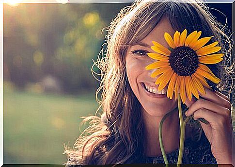 Girl holding a sunflower in front of her eye and smiling because your smile can change the world