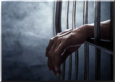 Two hands sticking through the bars of a prison